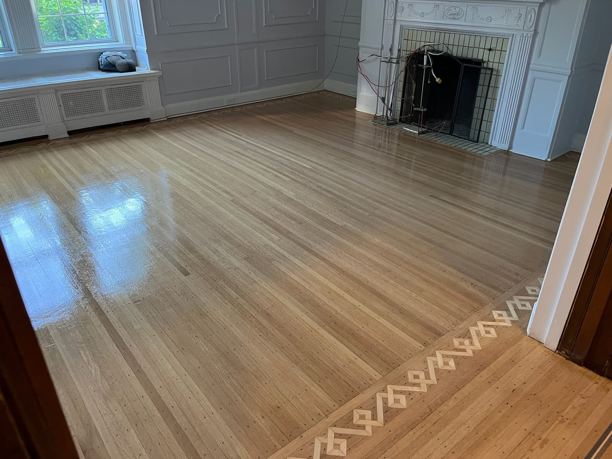 Plancher de chêne verni avec bordure décorative, près d’un foyer