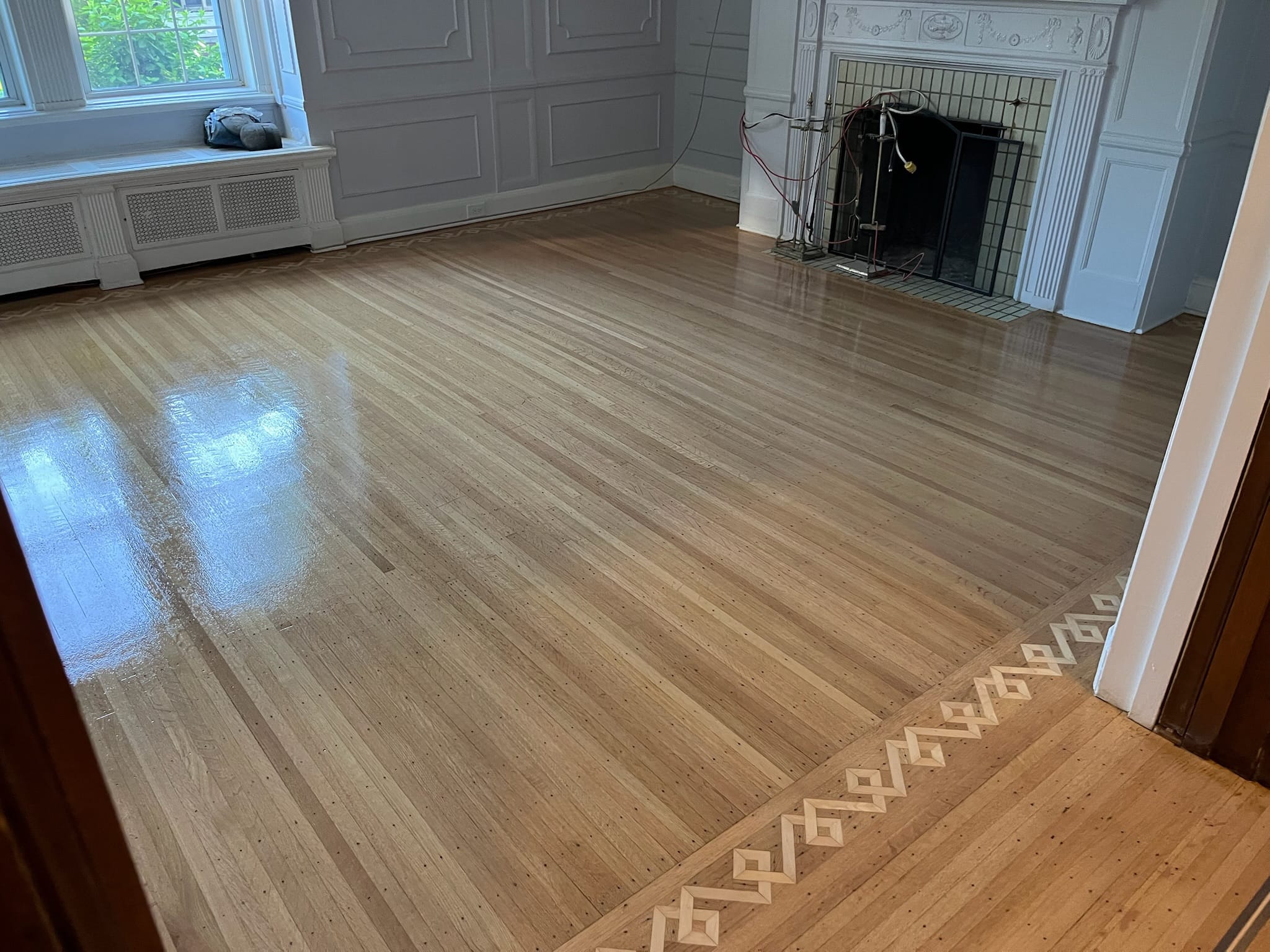 Plancher de chêne verni avec bordure décorative, près d’un foyer